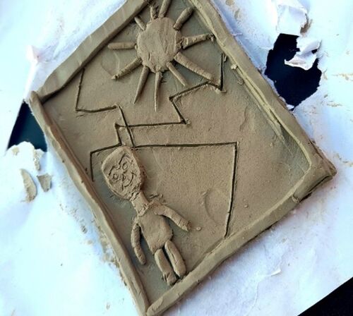 clay sculpture plaque featuring a person in bottom left and sun in top right corner separated through carved crack marks.