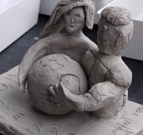 clay sculpture of man and woman embracing globe of earth