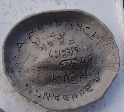 clay sculpture plate with "Abundance" carved towards edge and words "Fear", "Scarcity", "Rich", and "Poor" carved toward centre
