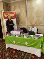 Gerry sitting at a table covered in copies of Working for Work with James standing next to the table
